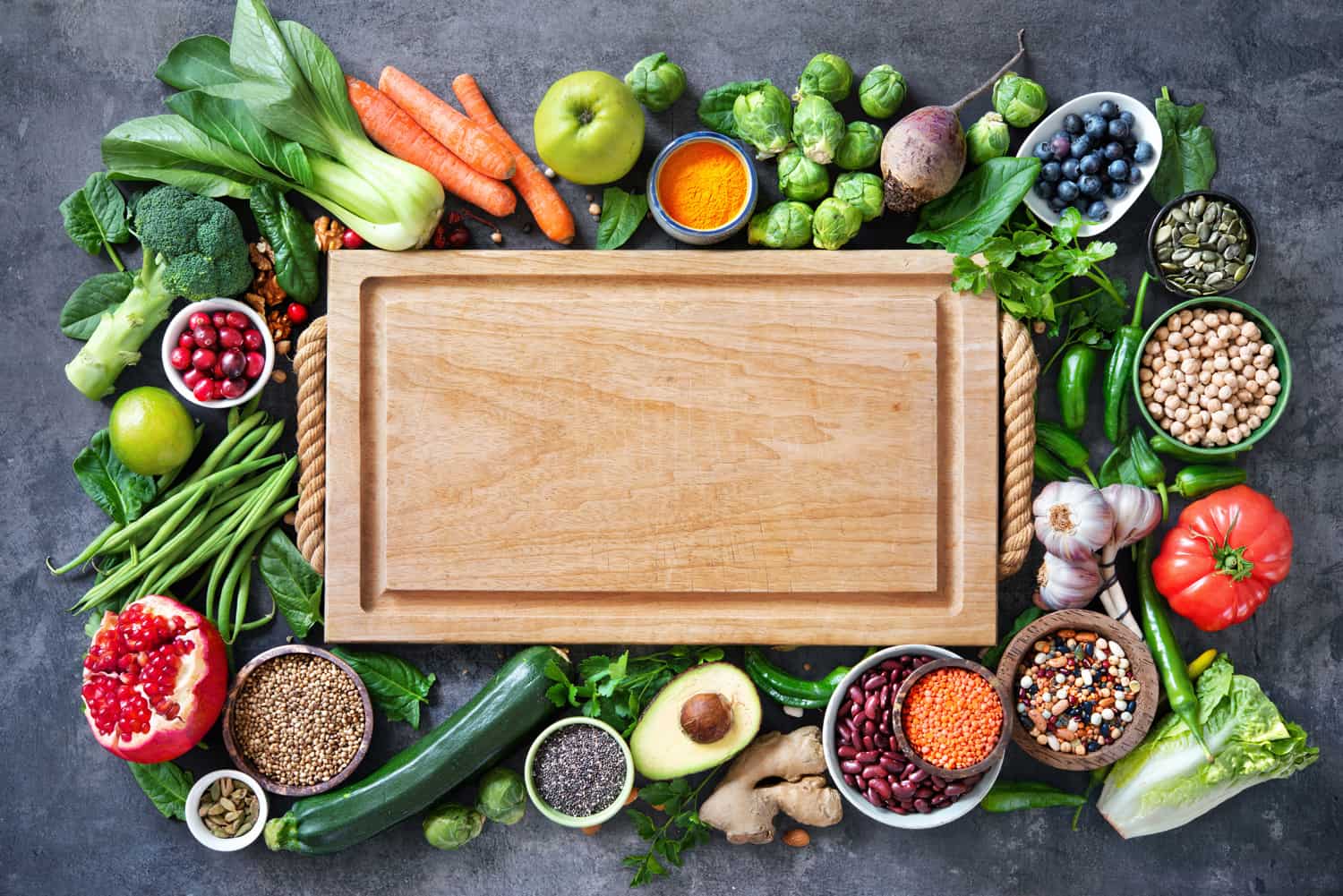Healthy food selection with fruits, vegetables, seeds, super foods, cereals and the cutting board in the middle as copy space