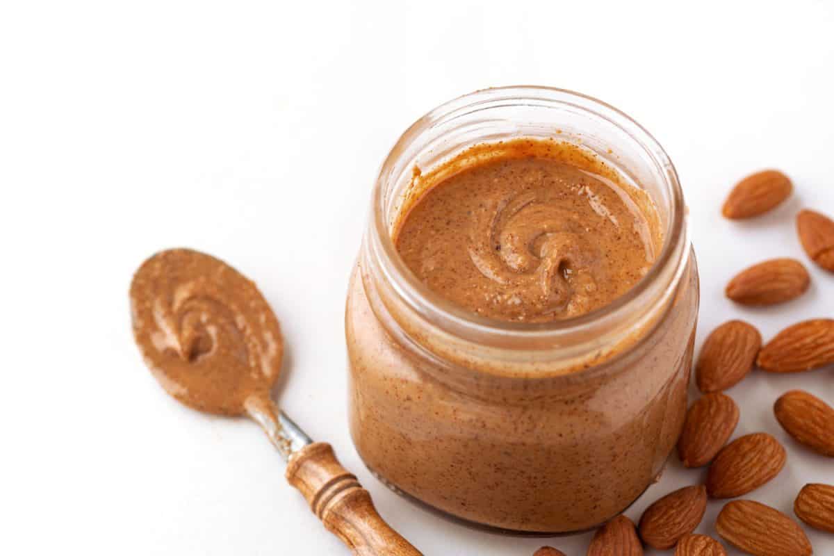Organic almond butter with raw almonds in a glass jar on a white background
