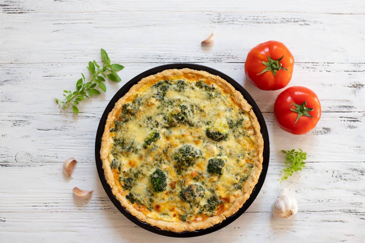 Perfectly cooked French quiche cooked on a small cooking plate with tomatoes on the side