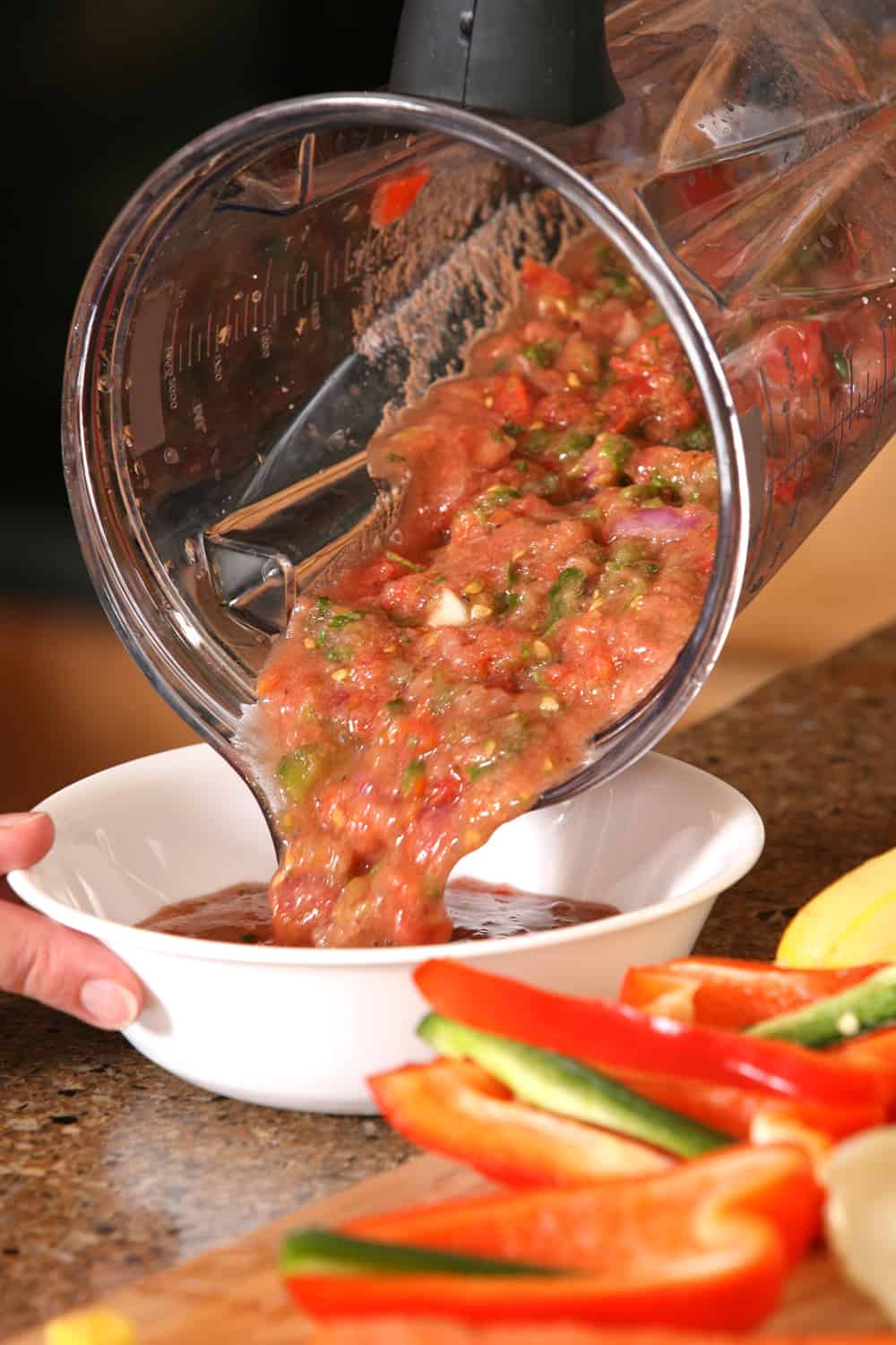 Salsa that was just made in a food processor is being poured into a bowl for serving.