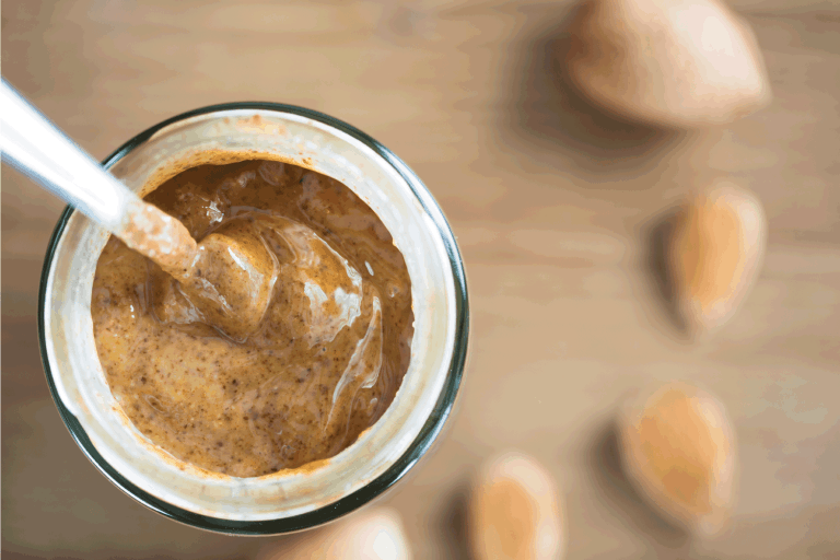 creamy Almond Butter in Jar with spoon, blurred background