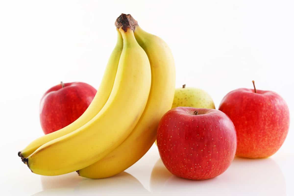 A banana placed next to apples on a white background