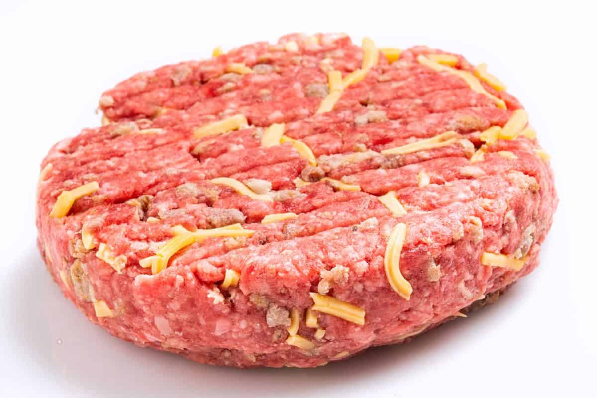 A big burger patty with small slices of cheese on a white background