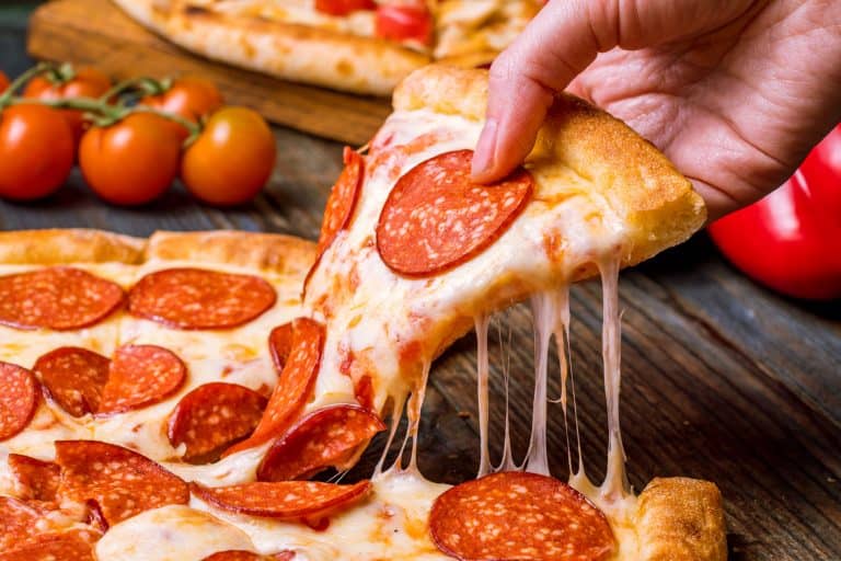 A woman taking a big slice of pepperoni, Does Pizza Go Bad If Left Out Overnight?