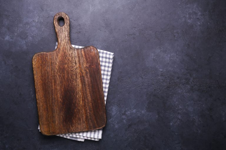 A wooden cutting board with a cloth under it, Does A Wood Cutting Board Hold Bacteria?