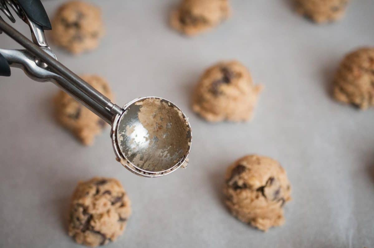 An overhead photograph of a baking pan with raw chocolate chip cookies dough and scoop