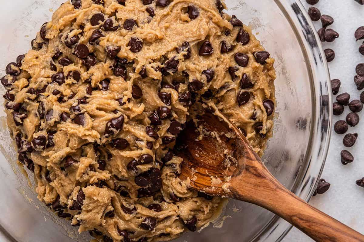 Chocolate chip cookie batter in a bowl with a wooden spoon and spilled chocolate chips