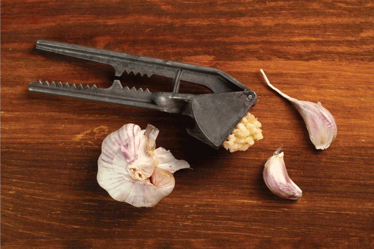 Garlic crushed and garlic press on a brown wooden table. 5 Garlic Press Alternatives To Try Our