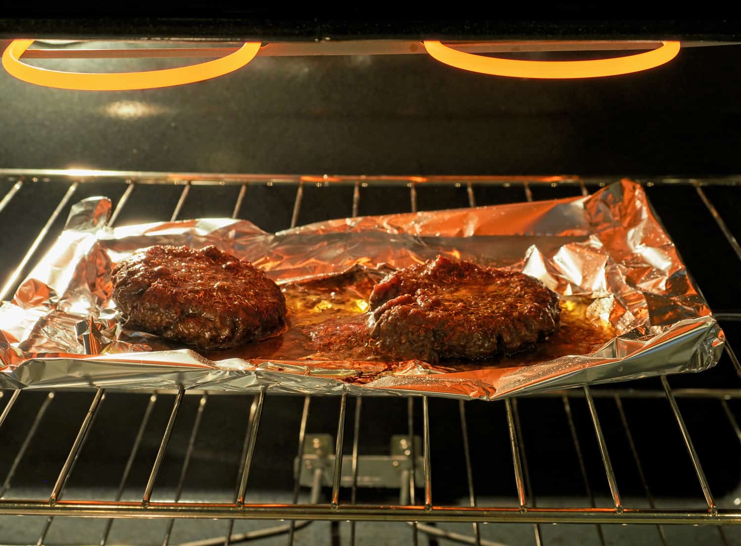Greasy hamburgers being broiled in an electric stove. Hamburger patties on an aluminum foil tray to collect the abundant unhealthy grease.