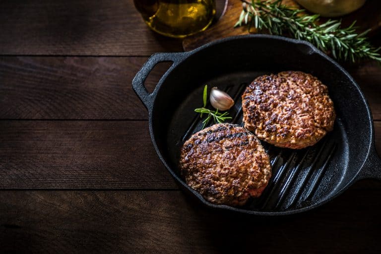 High angle view of a cooking pan with two grilled burger meats surrounded by a rosemary stick and an olive oil bottle on a rustic wooden table, How Big Are Hamburger Patties?