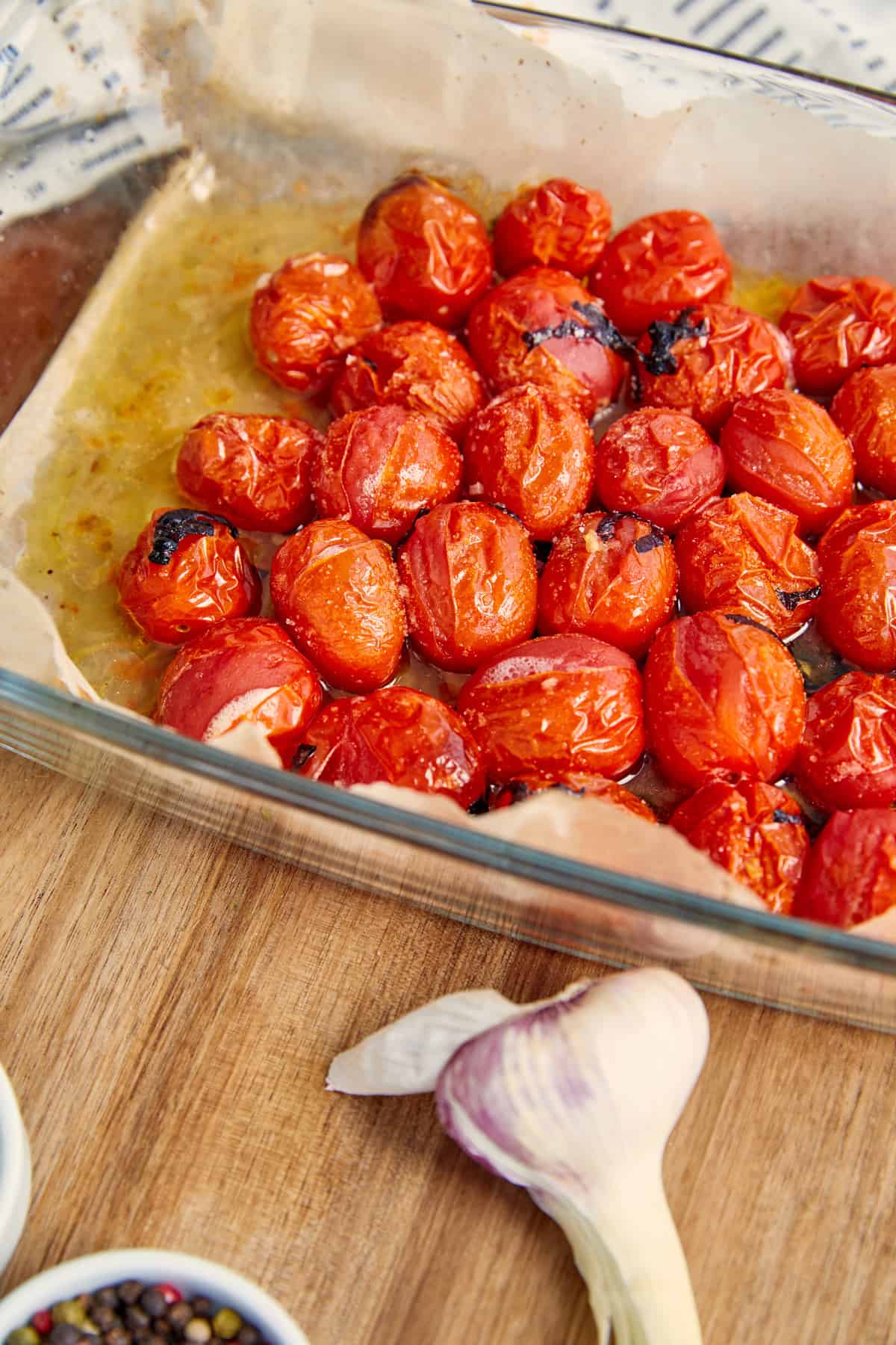 High angle view of prepared tomatoes in baking dish near garlic on wooden background