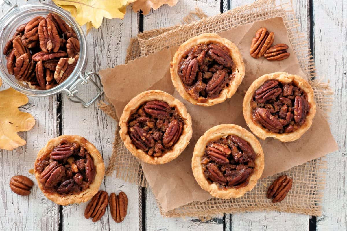 Mini pecan pie tarts, above view table scene on a rustic white wood background