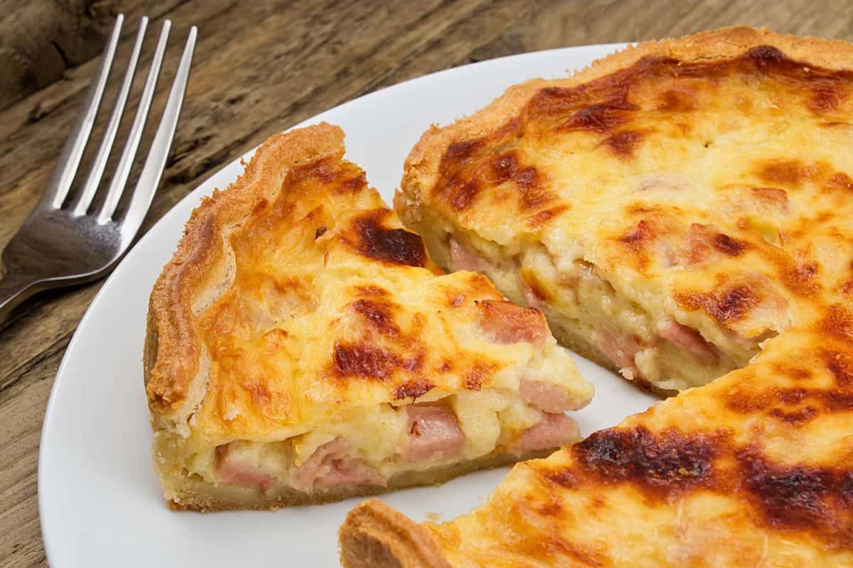 Portion of cheese and bacon flan cut from the quiche lorraine in a rustic traditional farmhouse setting