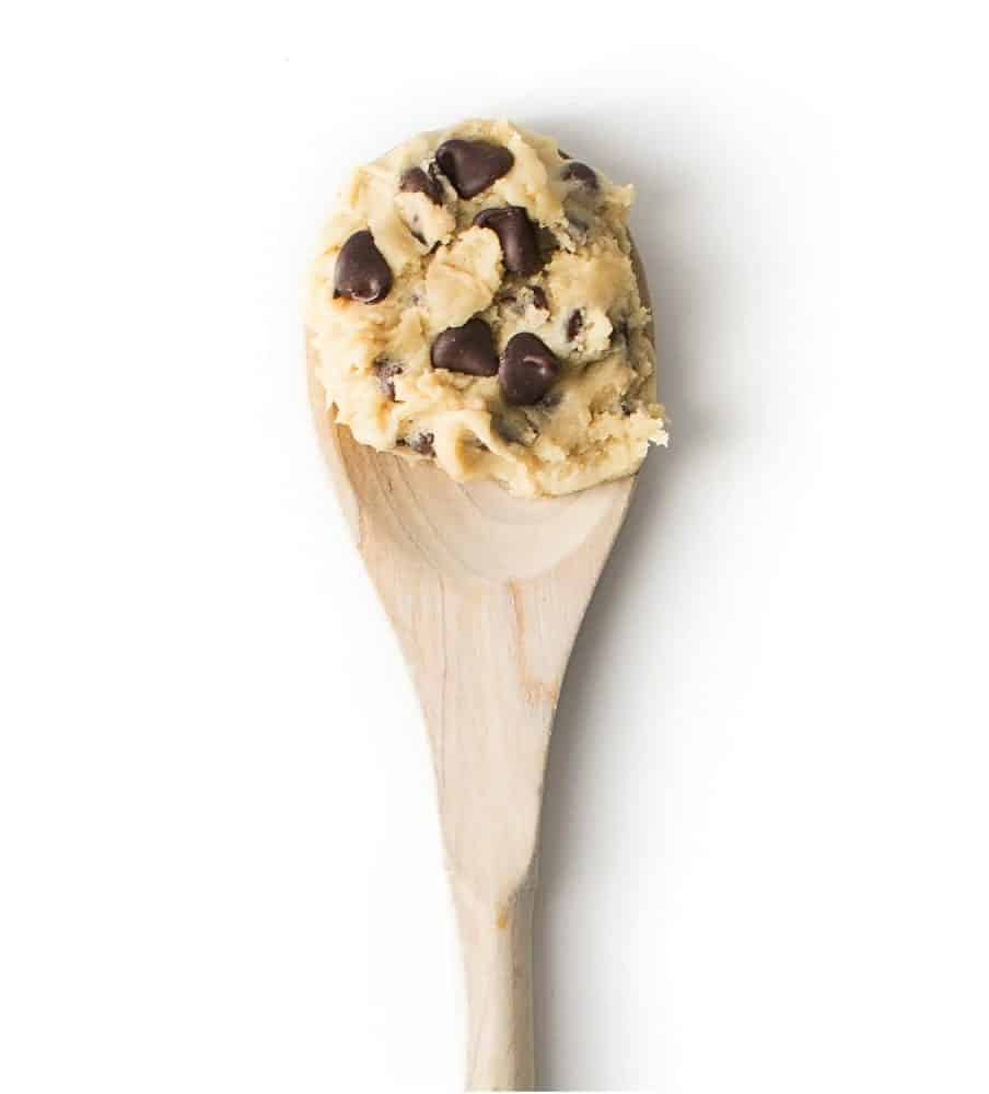 Raw cookie dough on a wooden spoon over a white background