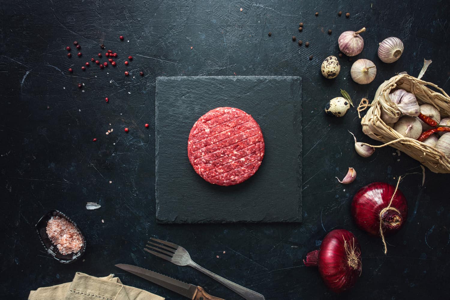 Raw minced beef burgers with spices layout on aged wooden cutting board. Directly above shot