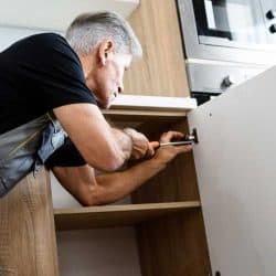 Repairman in uniform working, fixing kitchen cabinet using screwdriver, How To Restore Kitchen Cabinets And Fix Worn Spots