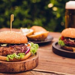Two delicious burgers with ranch dressing, lettuce, and cheese on a small wooden plate, How To Season Hamburgers For The Grill [9 Seasonings To Try Out]