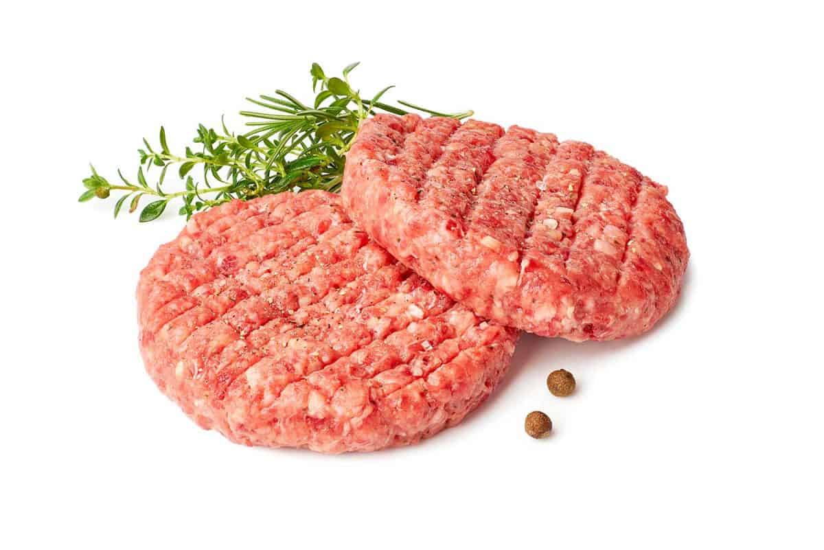 Two raw burger patties with thyme and rosemary