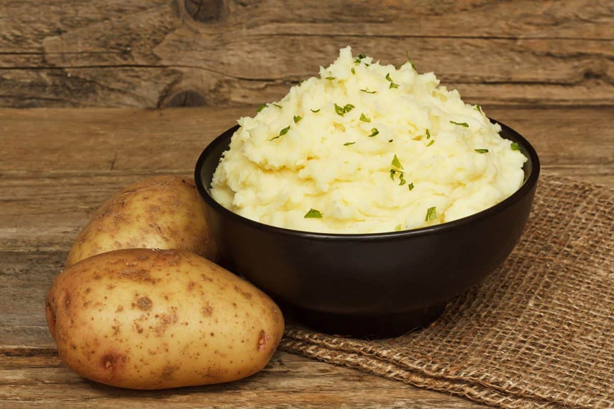 serving of creamy mashed potato made from boiled potatoes mixed with butter and served in a black bowl on a traditional rustic background