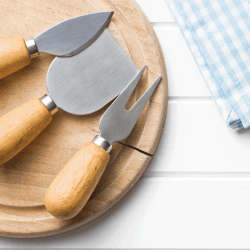 set of cheese knives on a round wooden board. 14 Types Of Cheese Knives [Inc. What Cheese They're Good For And Why]