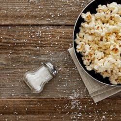 top view of delicious popcorn in frying pan near scattered salt on wooden background, 10 Types Of Oil For Popcorn To Consider