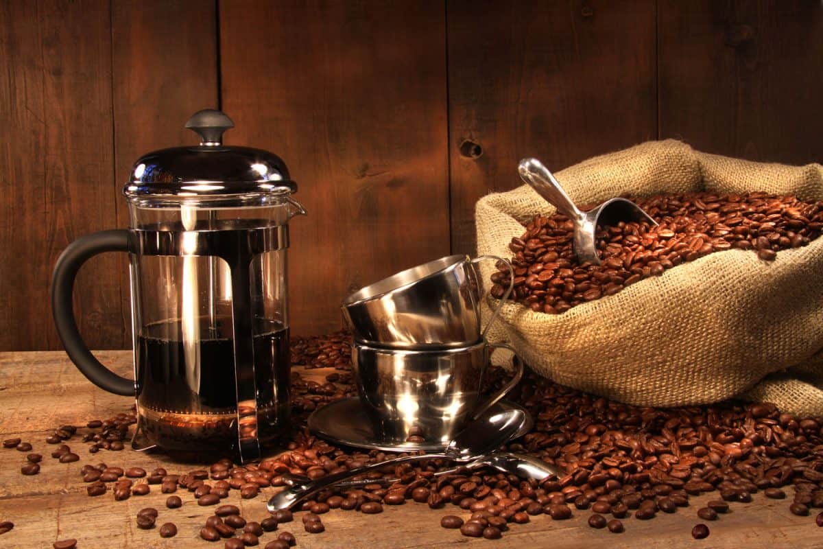 A French press with coffee next to coffee beans