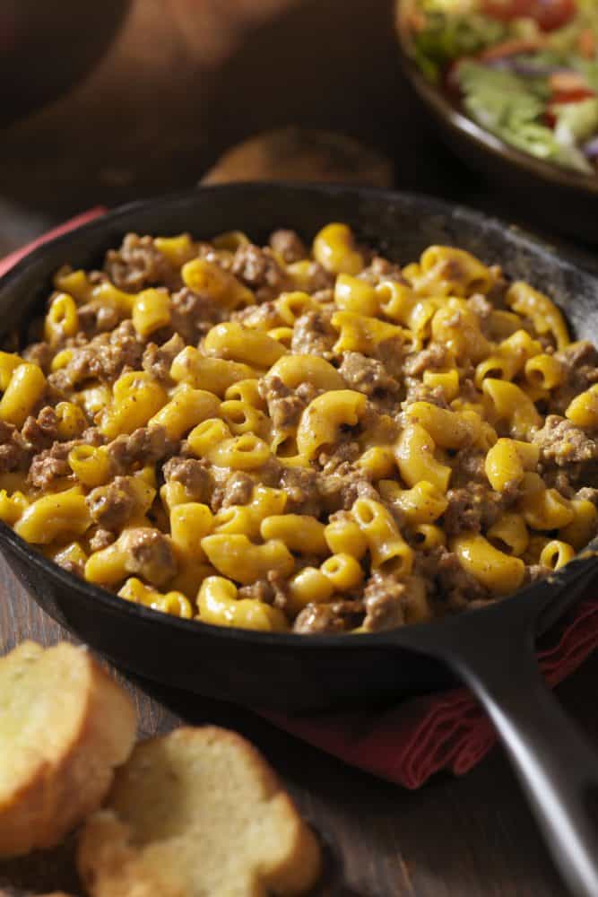 A cheesy hamburger with macaroni and cheese on a frying pan