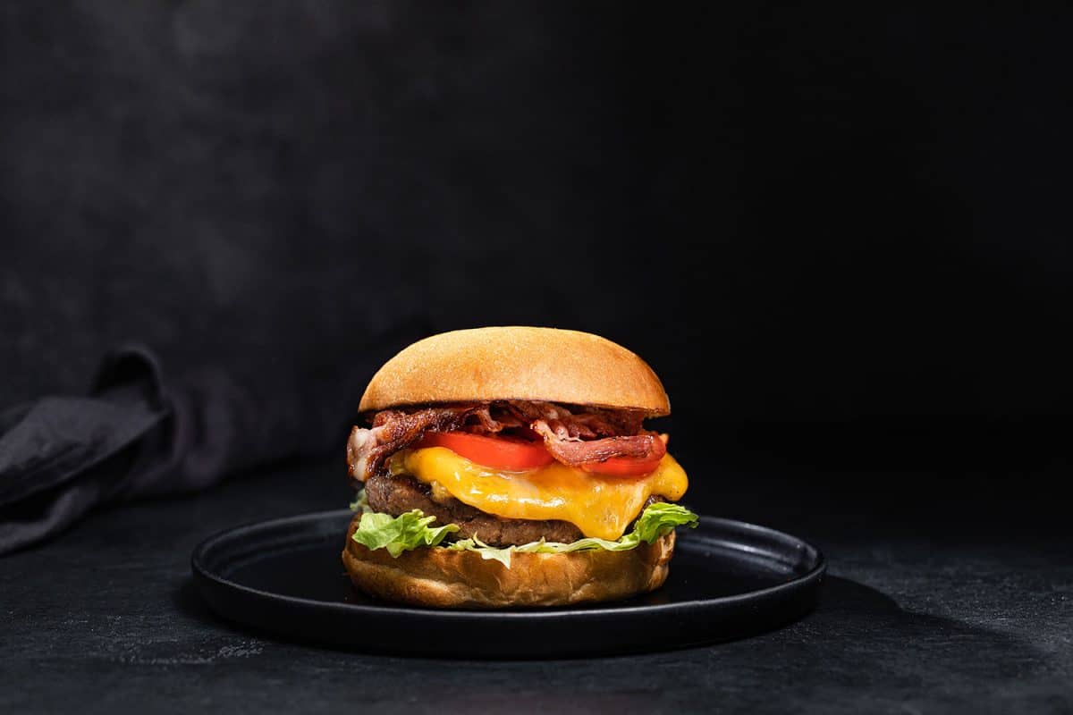 A hamburger composing of cheese, bacon, tomatoes, and lettuce
