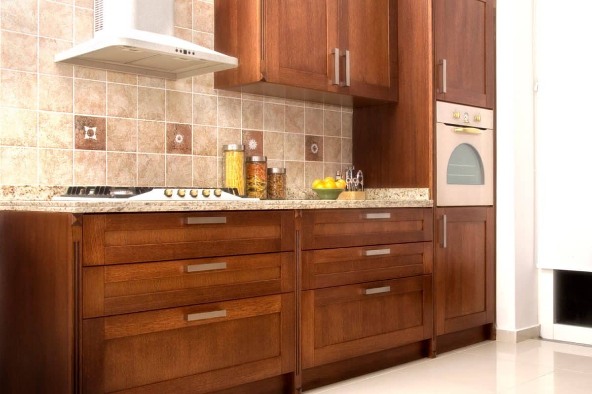 A kitchen with oak cabinetry brown tiled backsplash and a white rangehood, How To Adjust Kitchen Drawer Fronts