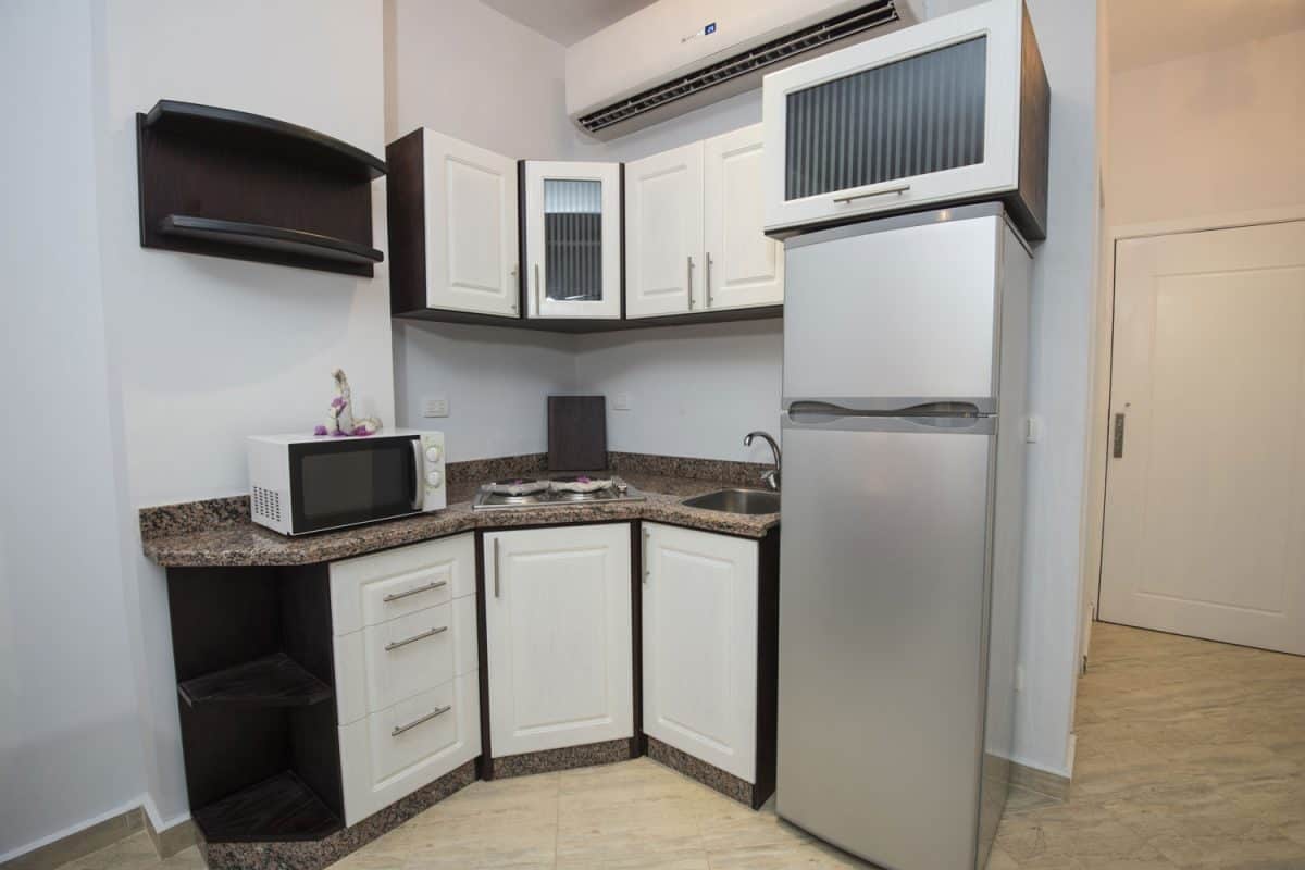 A small kitchen with a marble kitchen countertop, white kitchen cabinetry, and a microwave on top of the fridge