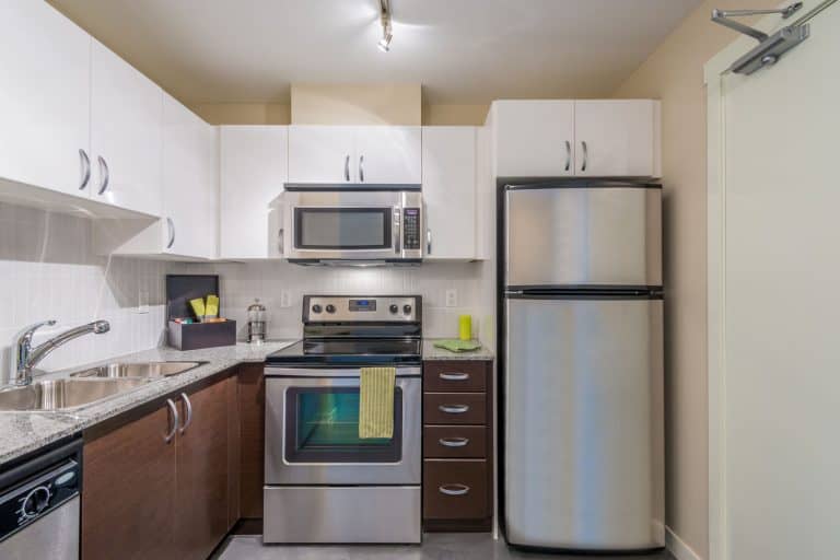 A small modern kitchen with oak cabinetries, white floating cabinets, and a microwave on top of the countertop, How Big is a Microwave? [By Type]