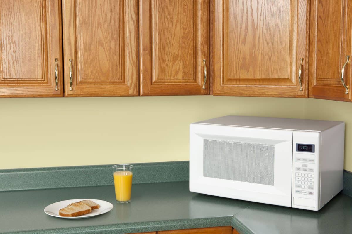 A white microwave inside a kitchen with a dark gray colored countertop