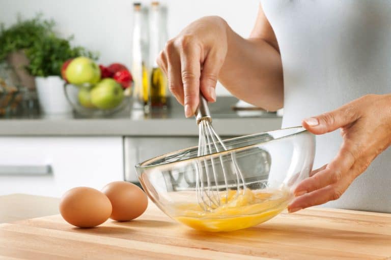 A woman Preparing food in her home kitchen, whisking eggs, Should You Whisk Scrambled Eggs? [The Secrets You Need To Know!]
