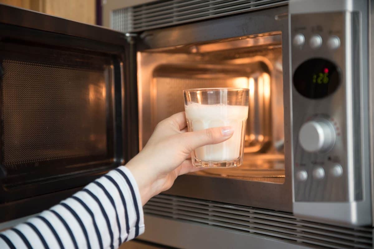 A woman putting a cup of milk into the microwave