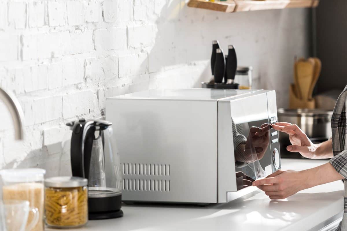 A woman putting a cup of milk into the microwave in the morning