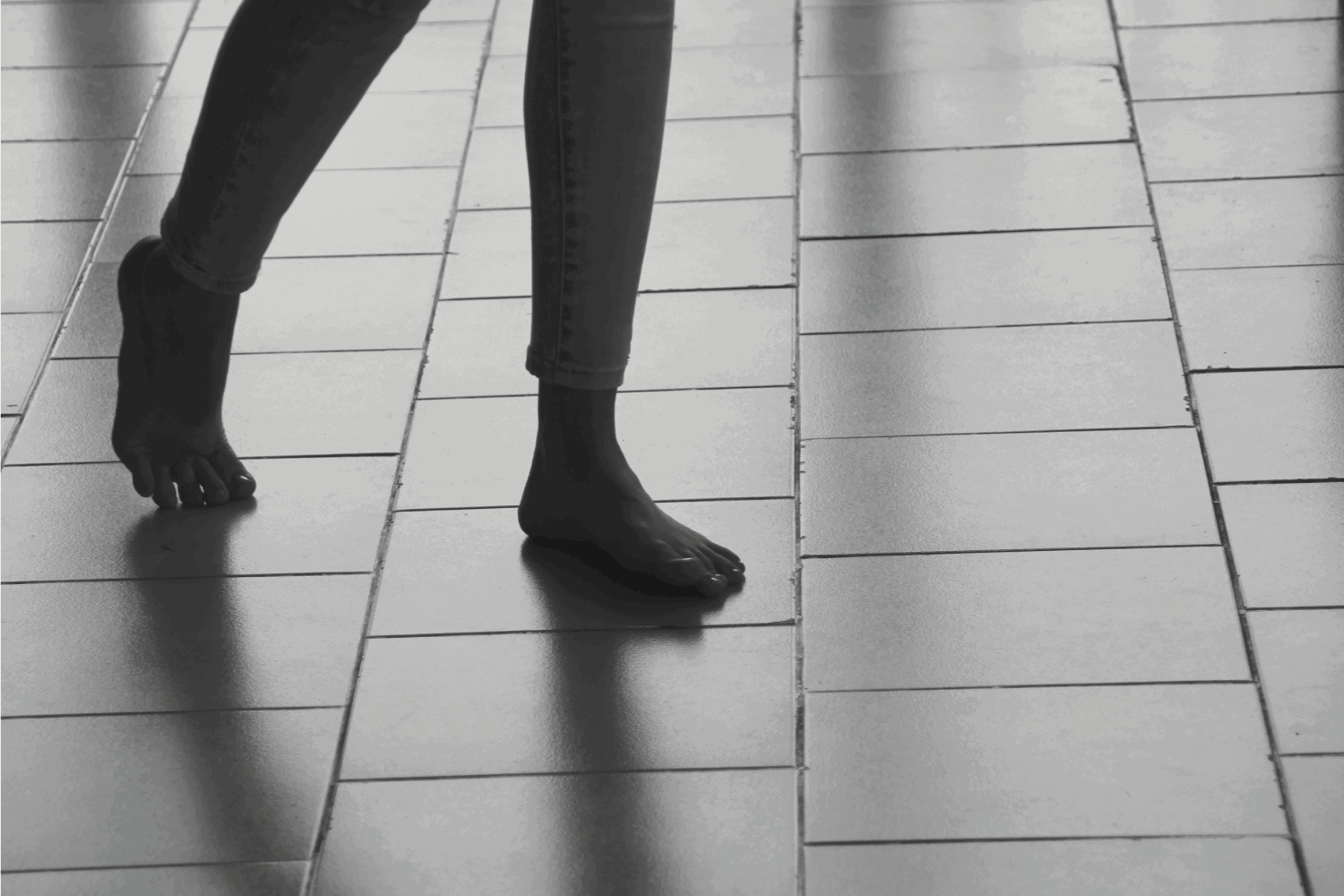 Abstract female feet go on tiled floor casting a shadows. The girl is walking barefoot on tile surface