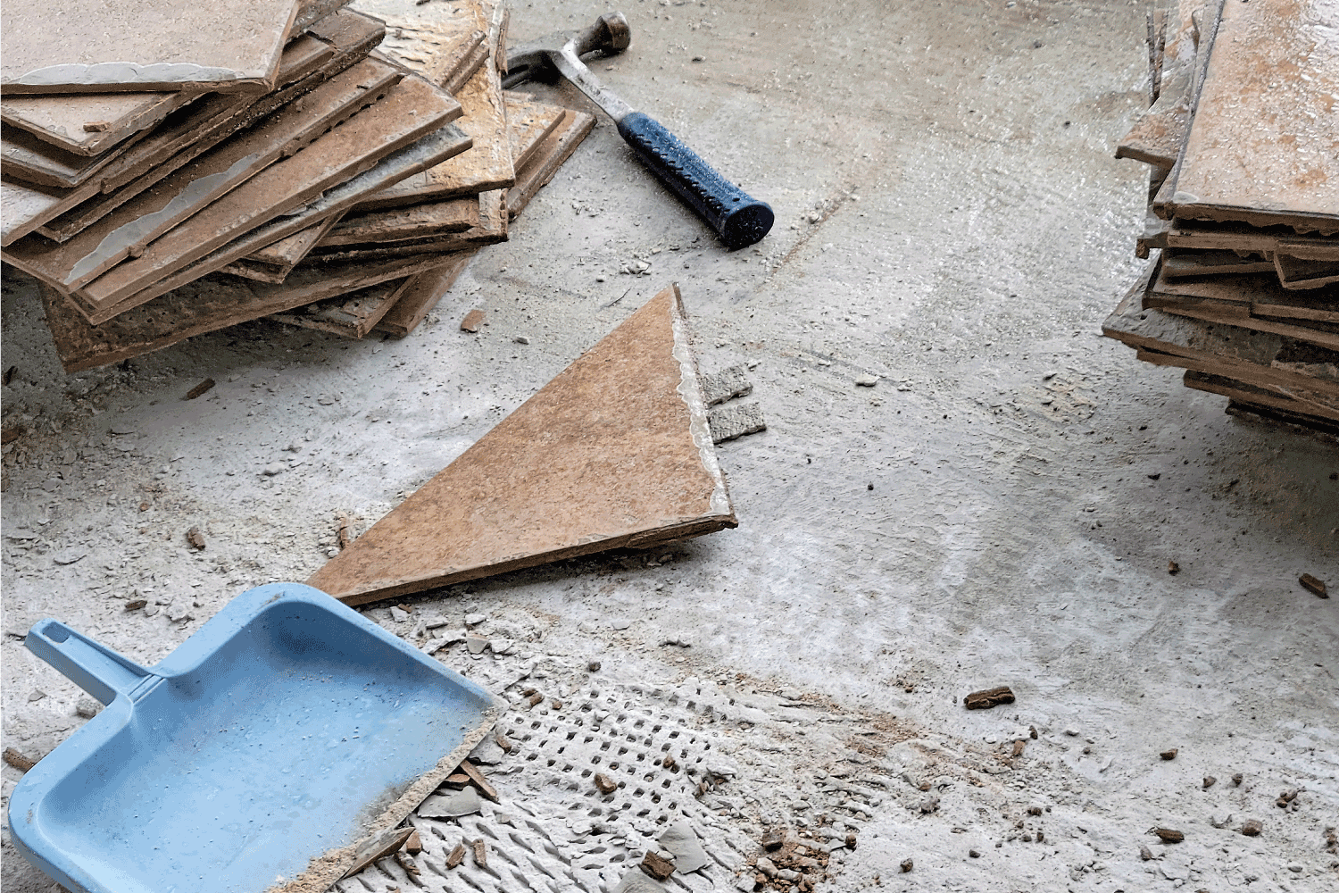Blue dustpan with a hammer and broken ceramic floor tile