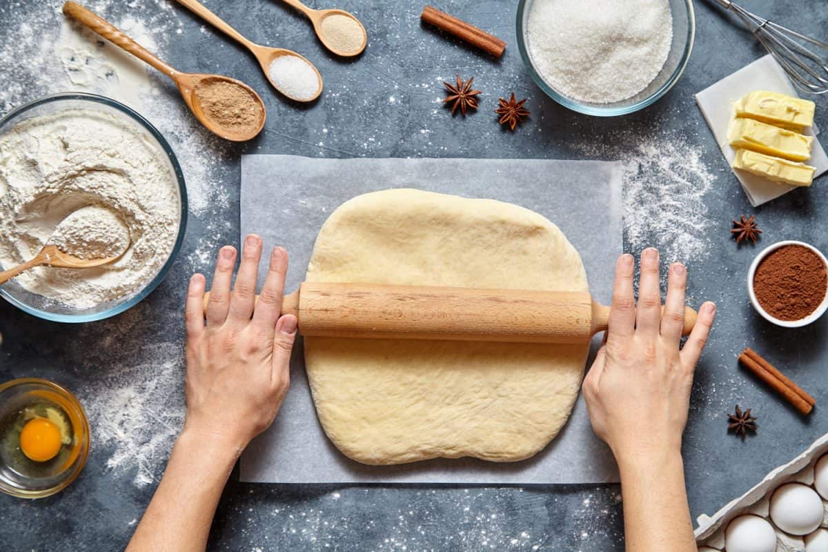 Dough bread, pizza or pie recipe traditional preparation. Female chef cook hands rolling dough with pin. Food ingridients flat lay on kitchen table. Working with pastry or bakery cooking. Top view