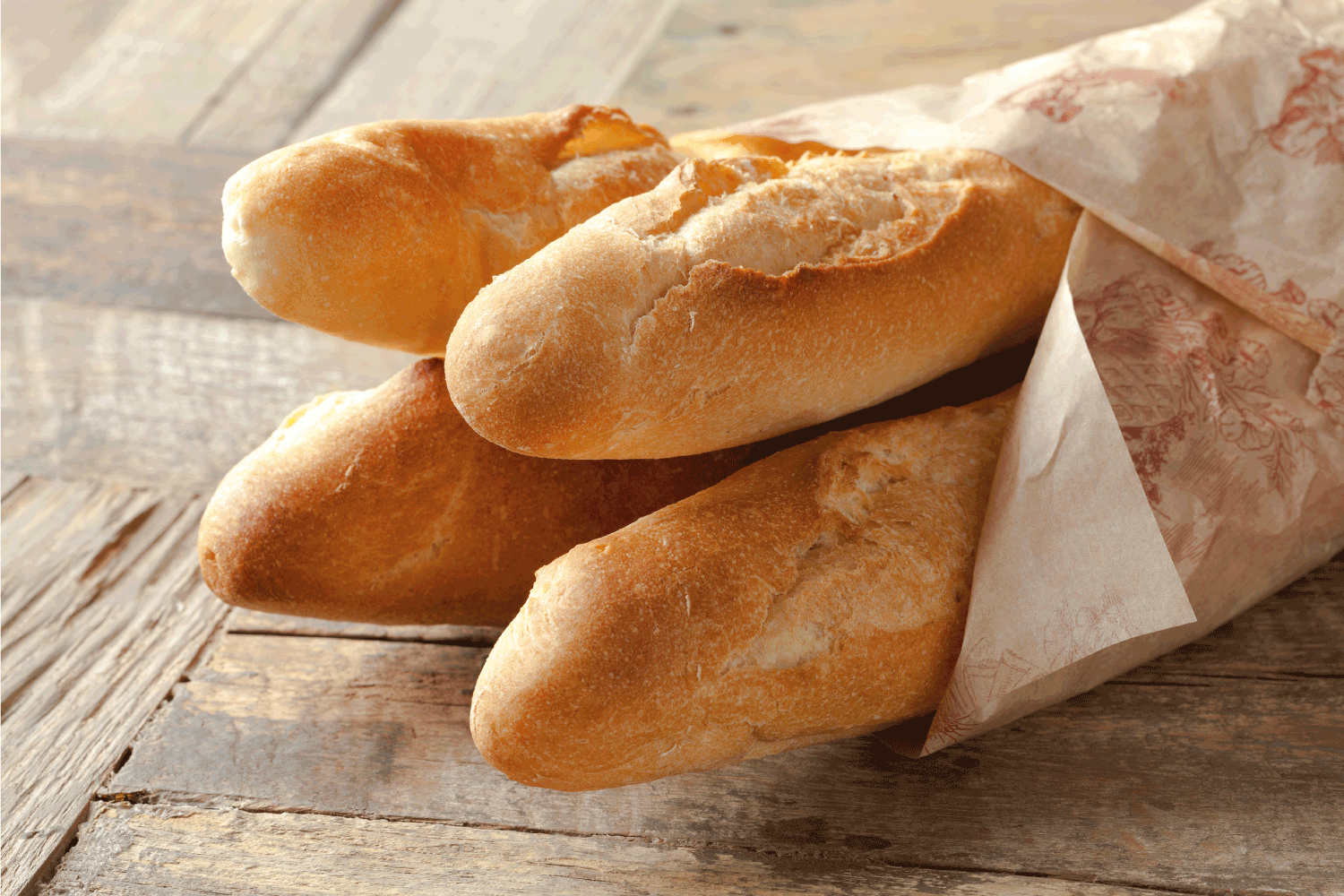 French baguettes wrapped in paper on top of a wooden table