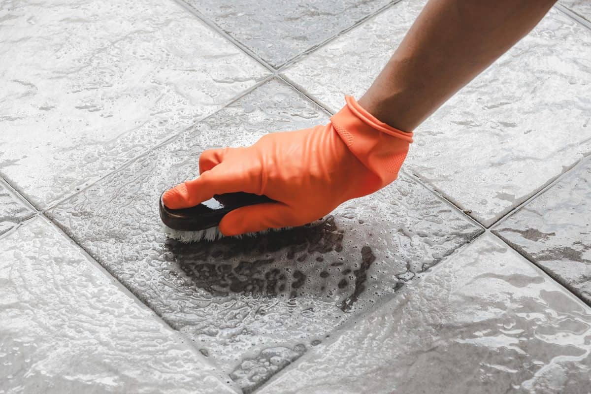 Hand of man wearing orange rubber gloves is used to convert scrub cleaning on the tile floor