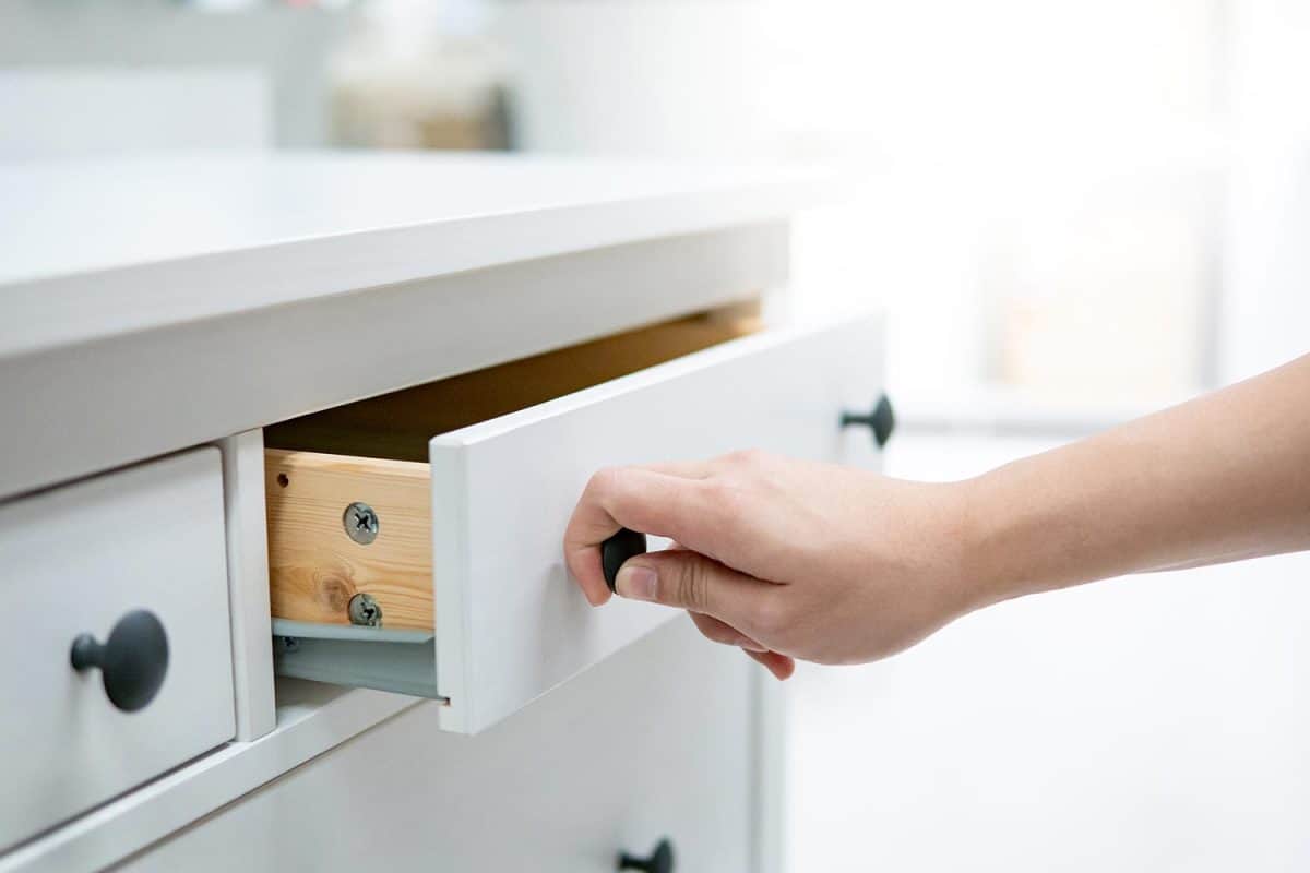 Male hand pulling and opening drawer on white wooden cabinet