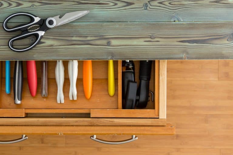 Neat line of colorful knives in a fitted drawer in a wooden kitchen cabinet with rustic counter top viewed from overhead with a pair of scissors or shears on top, Should You Paint The Inside Of Kitchen Drawers?