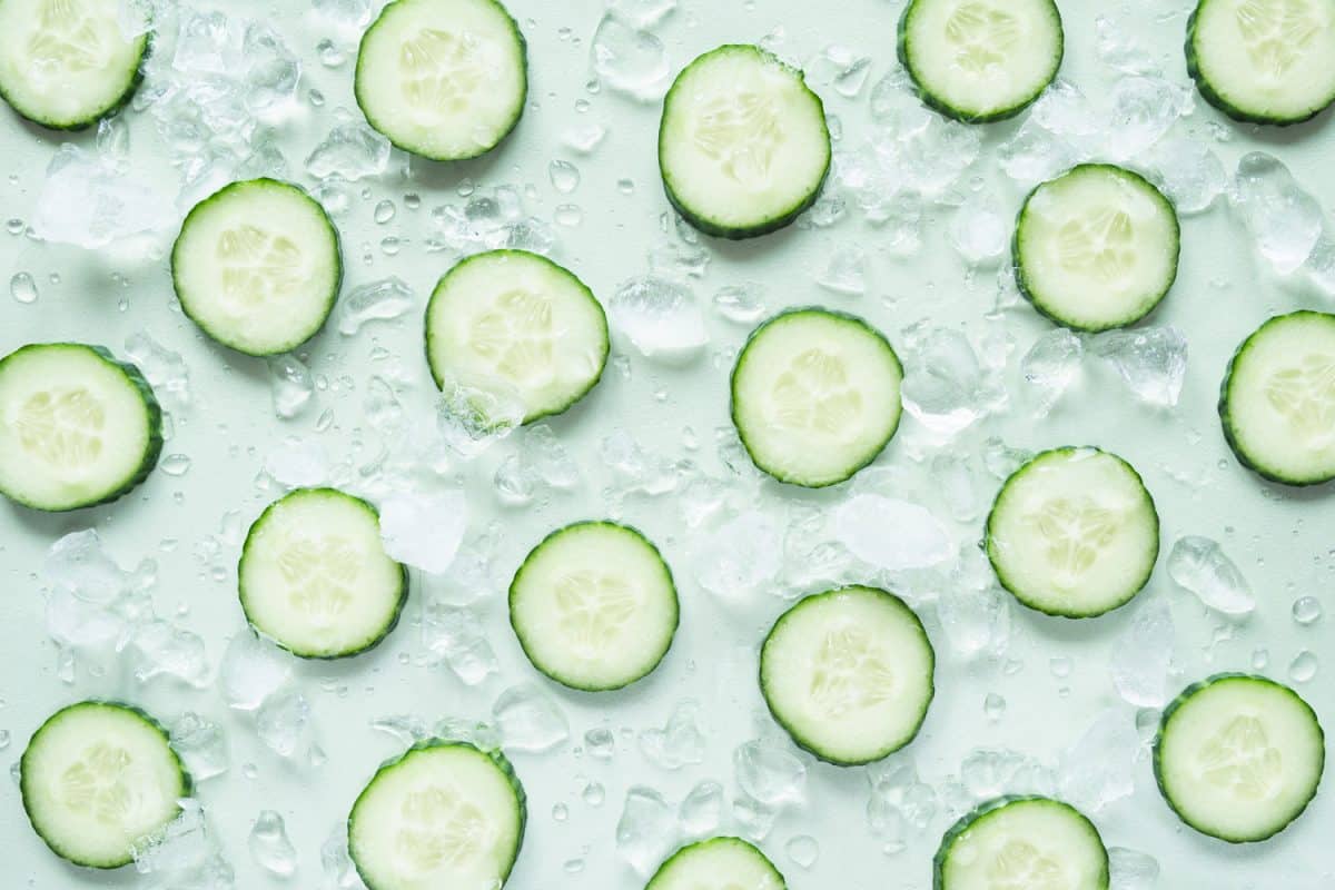 Pattern with freshly cut cucumber slices and ice cubes on light green background