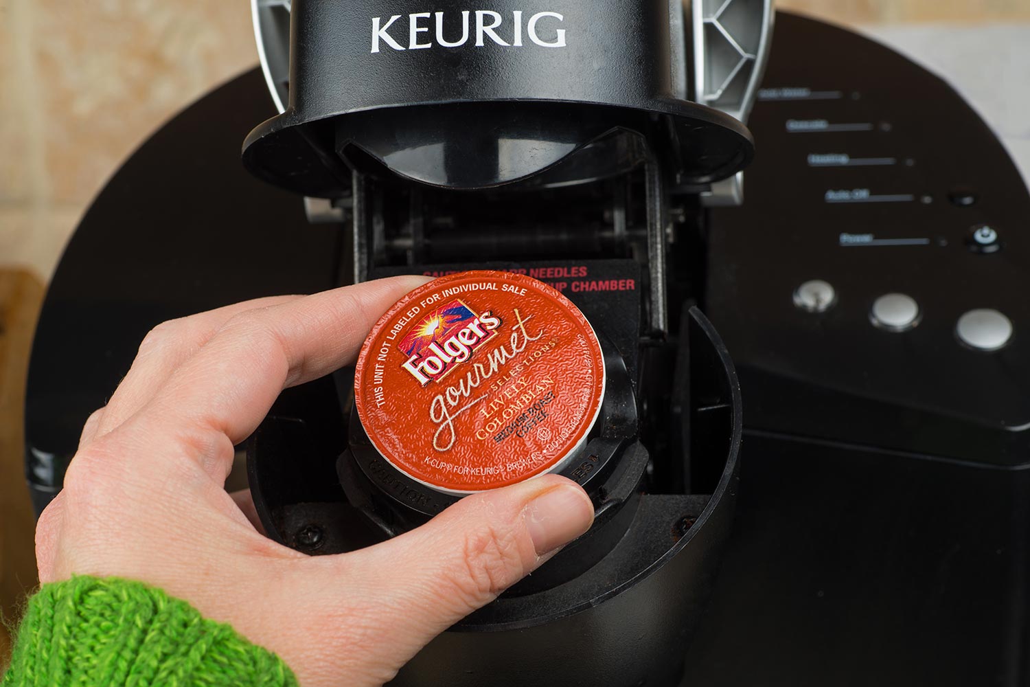 Woman inserting single-serve K-cup Foldger's coffee into a Keurig coffee maker
