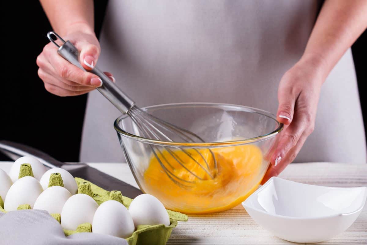 Young woman in a gray aprons breaks the eggs