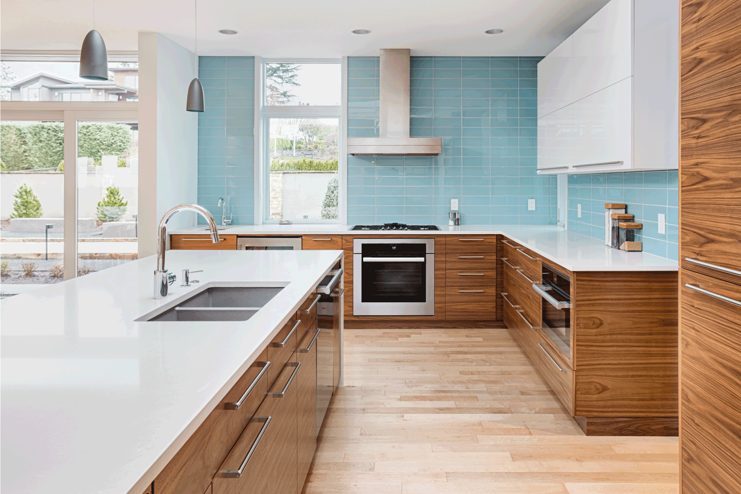 Beautiful modern kitchen in new contemporary style luxury home, with island, pendant lights, hardwood floors, and stainless steel appliances. Features blue tone tile that extends to the ceiling