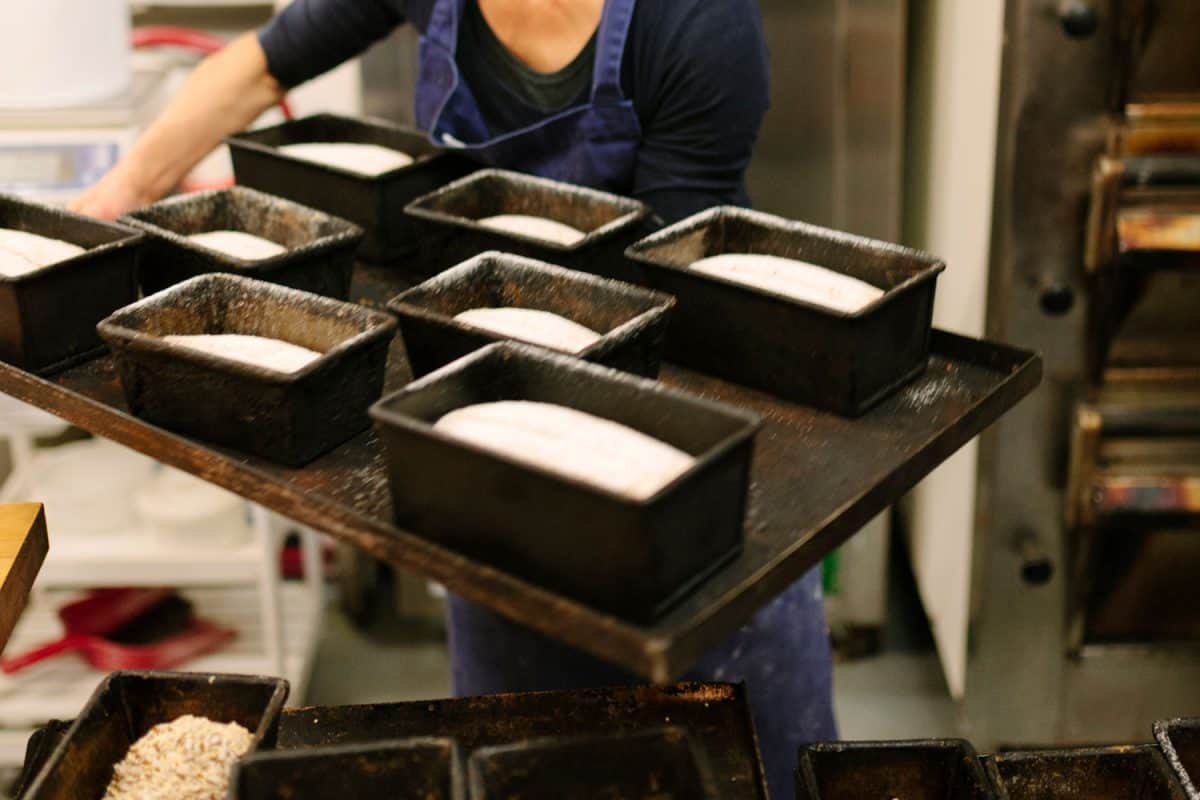 A baker moves trays of bread dough within loaf pans