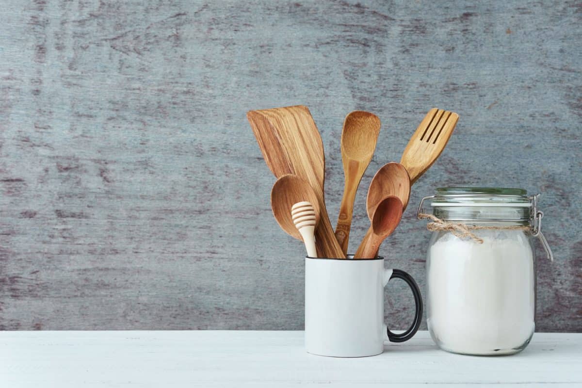 A ceramic mug with wooden utensils on it and a small jar with white sugar