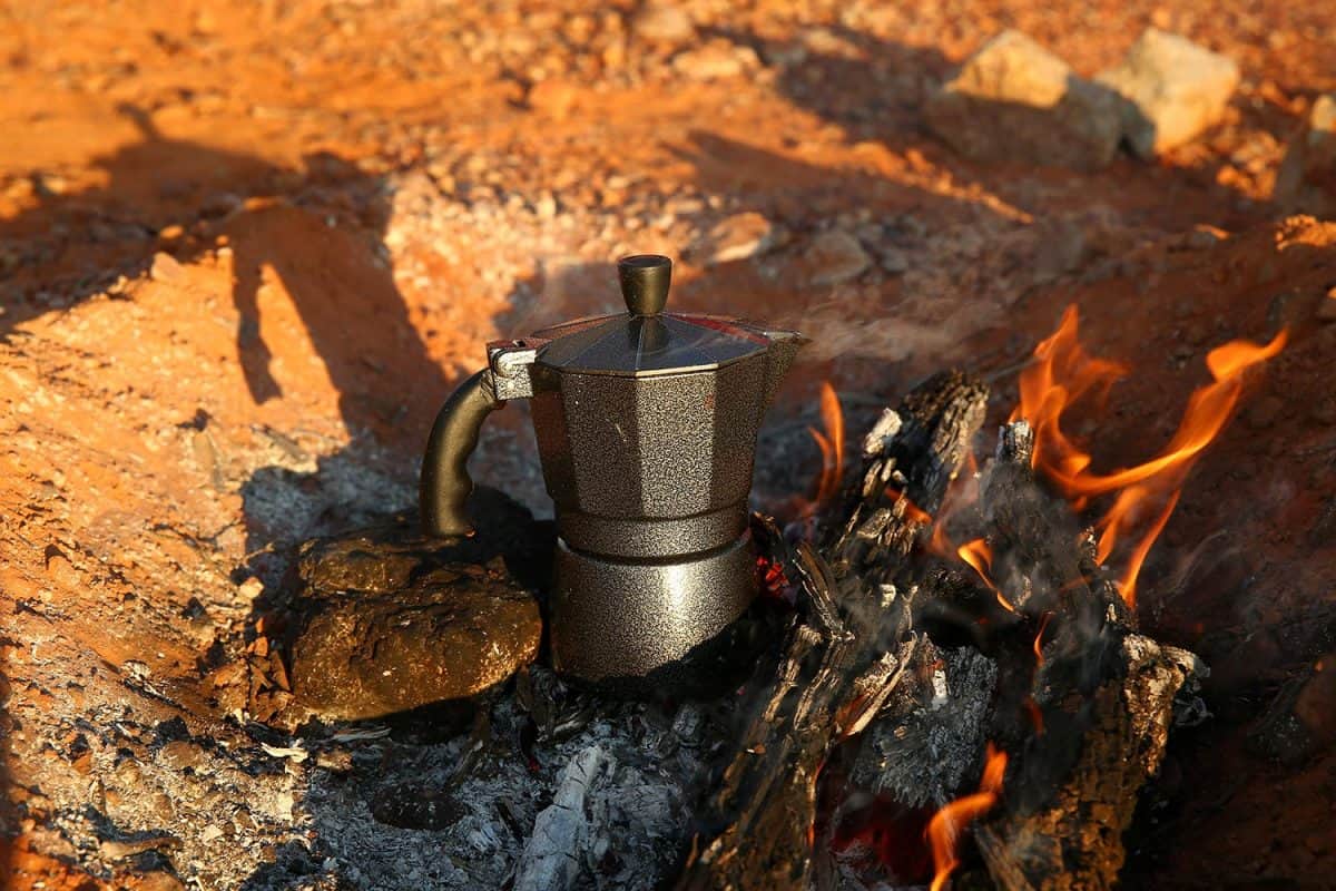 A shallow depth view of a stove top espresso coffee maker being used in a camp fire