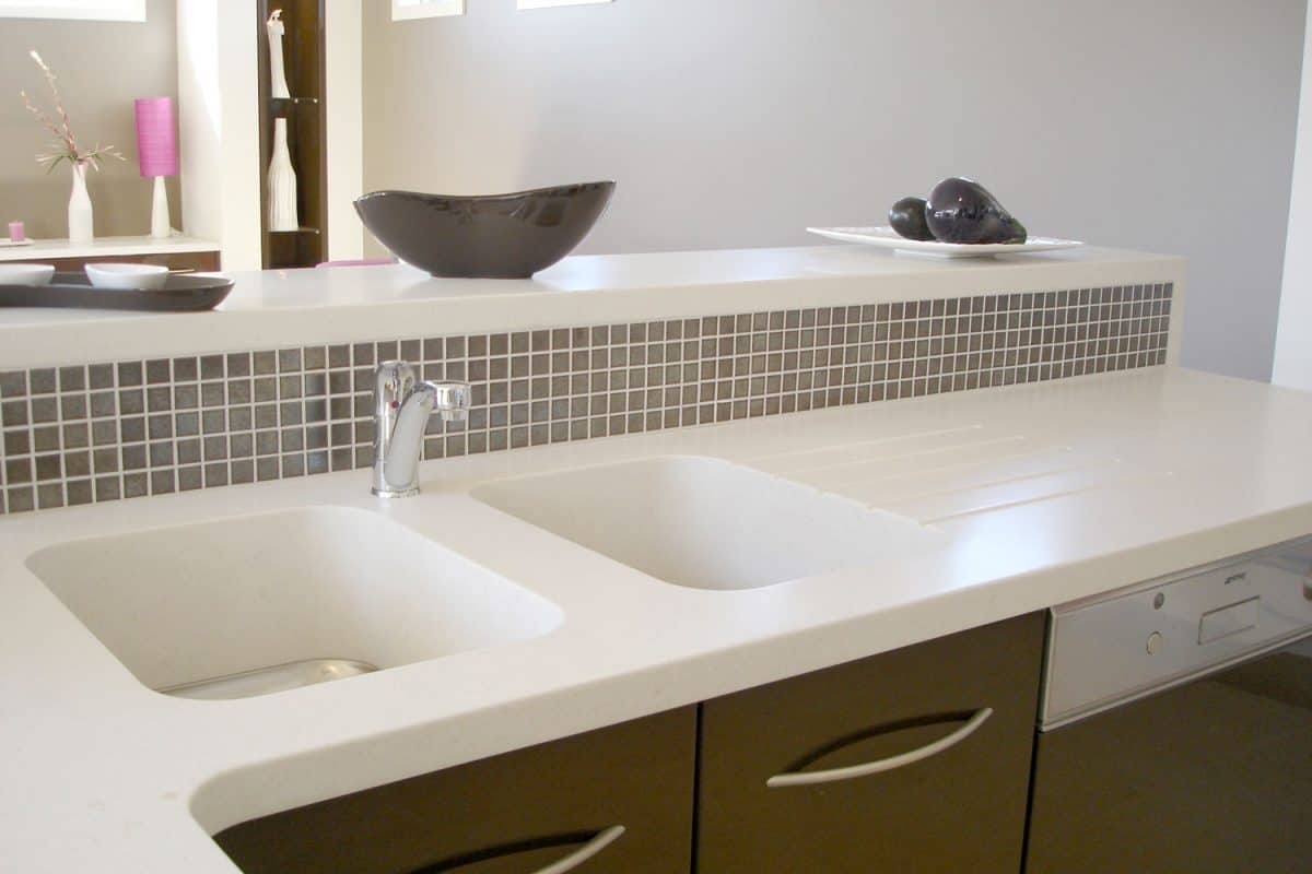 A white bathroom countertop with brown colored drawers and a huge mirror